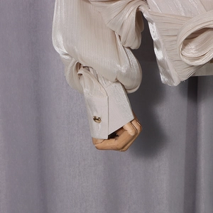 Close-up of pleated champagne satin sleeve with a polished gold button and refined texture