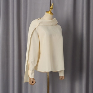 Detail of elegant cream blouse featuring irregular draped collar and split cuff design