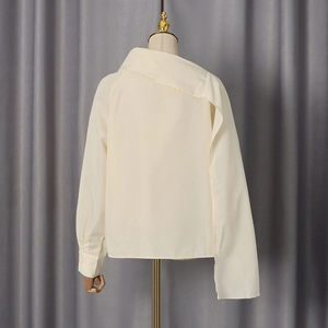 Detailed view of cream-colored blouse with asymmetrical collar and draped cape sleeve