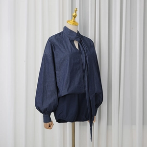 Detailed view of dark blue denim shirt with chic tie neck and puff lantern sleeves