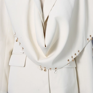 Detail of metal grommets and pearl pendants on elegant cream shawl collar blazer