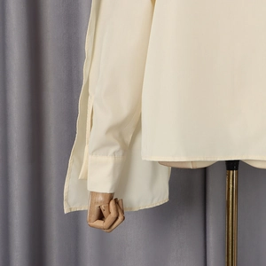 Detail view of cream-colored long sleeve shirt showing cuff stitching and side slit design