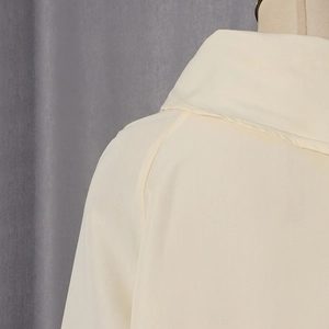 Detail view of the neckline and raglan sleeve stitching on the cream-colored blouse
