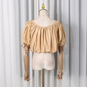 Close-up of beige puff sleeve top featuring pleated round neck and tie-cuffs on wood mannequin