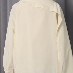 Detail view of cream asymmetrical layered fabric on the back of a stylish long sleeve shirt