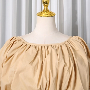 Detailed view of the gathered neckline and textured fabric on the beige pleated shirt