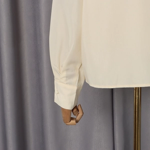 Detailed close-up of beige shirt cuff and sleeve fabric texture on a wooden mannequin