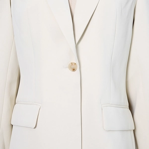 Detail of cream blazer with marble-patterned amber button and textured woven fabric