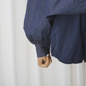 Detail of light blue denim lantern sleeve cuffs with refined stitching and drape