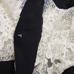 Détail macro de la broderie en dentelle florale et du crochet métallique sur la veste