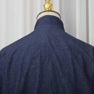 Close-up of reinforced back collar stitching on dark blue denim shirt with twill texture