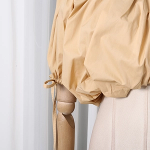 Detail of adjustable drawstring cuffs and pleated puff sleeves on a beige cotton blouse