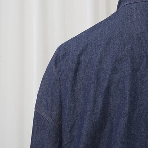 Detailed view of dark denim shirt shoulder with orange contrast stitching and twill texture