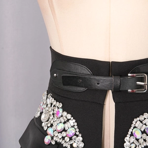 Detail of the high-waisted black skirt featuring sparkling rhinestones and a leather belt