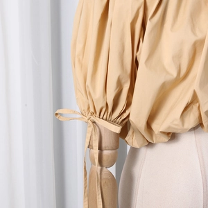 Detail of puff sleeves and ribbon bow on beige irregular cropped shirt for women
