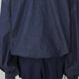 Detail view of dark blue denim shirt back featuring puffy sleeves and an elastic hemline