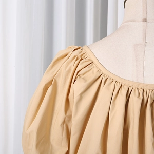 Detail of khaki puff sleeve blouse featuring a wide round neckline and pleated shoulders