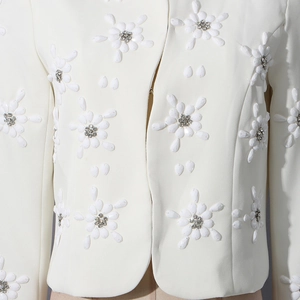 Detail of white blazer with 3D floral appliqués and rhinestone centers in close-up view