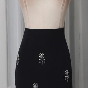 Detailed view of black high-waisted skirt with hand-sewn rhinestone flowers and pearls