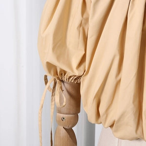 Detailed close-up of drawstring cuffs and pleated texture on apricot puff sleeve shirt
