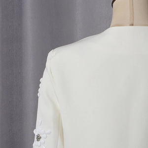 Detail of white blazer sleeve featuring 3D floral petals and sparkling rhinestone centers