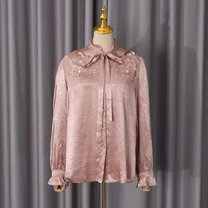Detailed view of dusty pink satin shirt featuring sequined shoulders and bow neckline