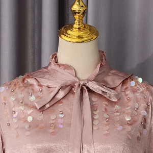 Detail of mauve satin shirt with ruffled neck, bow tie, and sparkling sequins on shoulder
