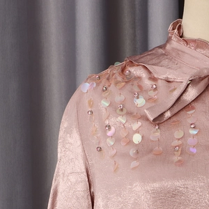 Detail of pink satin shirt with ruffled collar and sparkling sequins on shoulder