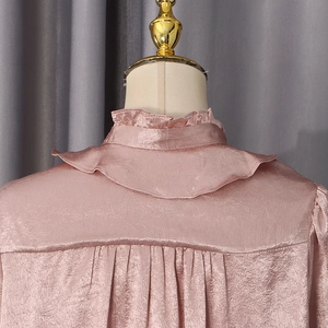 Detail of pink pleated stand collar and ruffled edges on satin blouse fabric
