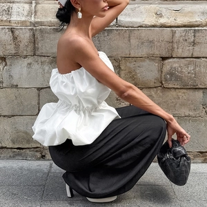 Détail d'un haut bustier blanc à volants et d'un pantalon large noir sur mur de pierre