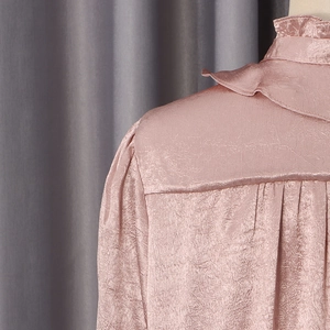 Detail of mauve pleated satin blouse with ruffled stand collar and textured fabric surface