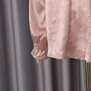 Detail of light pink pleated satin shirt cuff with frill edge and single button closure
