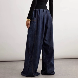 Detail of dark blue wide-leg jeans with orange contrast stitching and pleated waistline