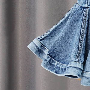 Detail of layered ruffle hem on light blue denim vest with acid wash finish