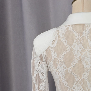 Detailed view of white lace bodysuit featuring sharp padded shoulders and floral patterns