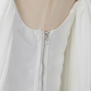 Close-up of silver metal zipper on white pleated bodice with sheer mesh paneling