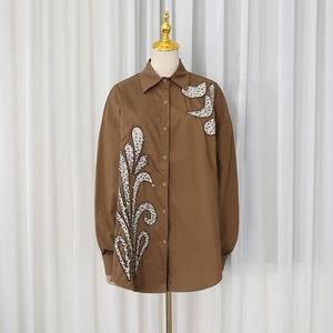 Detail of dark brown shirt featuring elegant white sequin leaf embroidery and buttons