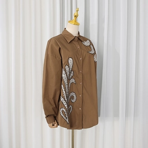 Macro detail of leaf-shaped sequin embroidery on a brown long-sleeve cotton shirt