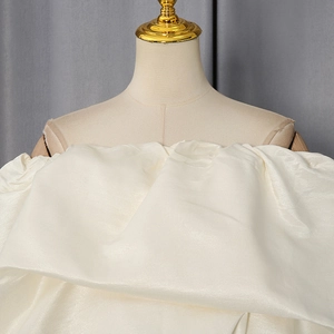 Detail of elegant white off-shoulder corset top in satin fabric with large pleats