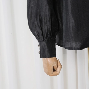 Close-up of black satin shirt cuff with lantern sleeve and pearl button details