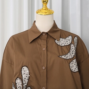 Detail of sequin embroidery and sparkling floral appliques on a brown long sleeve shirt