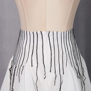 Detail view of white skirt featuring black vertical fringe and invisible zipper closure