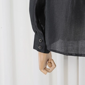 Detail of sheer black shirt sleeve featuring decorative double-button cuffs and texture
