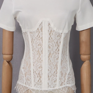 Dettaglio di un top a corsetto bianco con inserti in pizzo floreale e bordo a ciglia