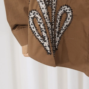 Detail view of heart-shaped sequins and white embroidery on brown long sleeve shirt
