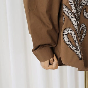 Detailed view of intricate sequin embroidery on a dark brown long sleeve shirt fabric