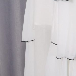 Detail of white mesh skirt featuring elegant black contrast stitching and wavy hem finish