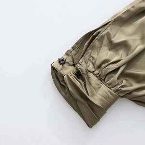Détail de la manchette en satin vert olive avec plis fins et deux boutons noirs