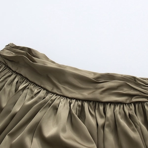 Détail du pantalon en satin vert olive avec plis à la taille et fermeture éclair invisible