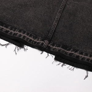 Dettaglio dell'orlo della gonna in denim scuro con bordi sfrangiati e nastro geometrico